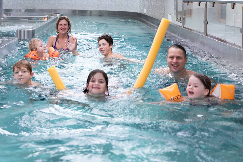 Familie schwimmt im Strudelino im Hallenbad